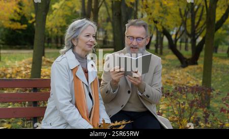 Vecchia coppia anziana anziana anziana donna matura uomo famiglia caucasica intelligente pensionato donna libro lettura poesie leggere letteratura sulla panchina in marito parco Foto Stock