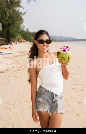 Giovane bella donna asiatica sorridente con la noce di cocco sulla spiaggia Foto Stock