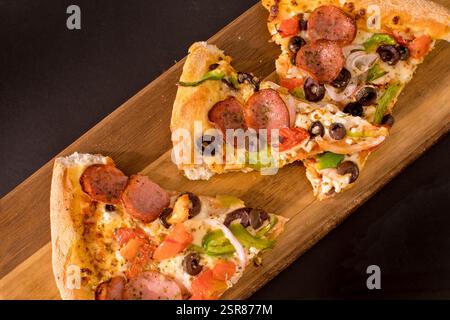 Fette di pizza tradizionale con salsiccia, funghi, peperoni, pomodoro, olive, formaggio e cipolla su un tagliere rustico in legno Foto Stock