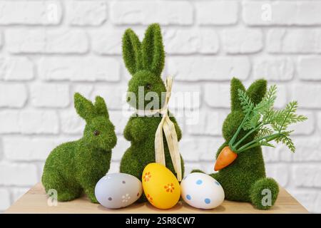 Personaggi decorativi a forma di coniglio con muschio verde con uova di Pasqua colorate su un tavolo in legno su sfondo bianco in mattoni. Vacanze di Pasqua, atmosfera festosa, Foto Stock
