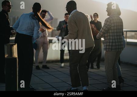Team di lavoro diversificato che festeggiano sul tetto al tramonto Foto Stock