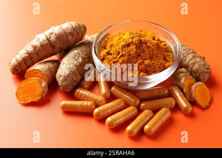 Polvere di curcuma in ciotola, radici e capsule su sfondo arancione, primo piano Foto Stock