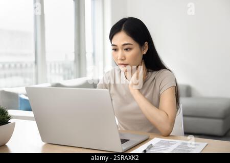 Giovane donna asiatica seria sedersi a tavola e usare il laptop Foto Stock