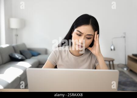 Donna seduta al suo notebook, che sembra preoccupata o stressata Foto Stock