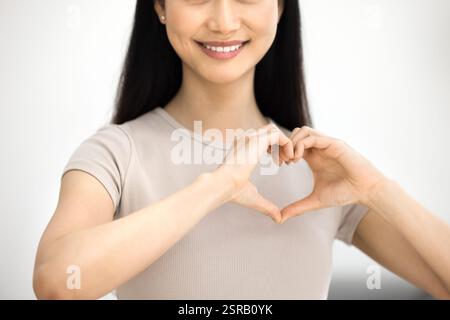 Donna asiatica sorridente che forma forma forma il cuore con le sue mani Foto Stock