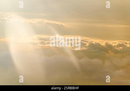 La luce soffusa del sole illumina le soffici nuvole, creando una tranquilla tonalità dorata. La vista aerea cattura la tranquilla atmosfera mattutina. I gradienti delicati evocano la calma A. Foto Stock