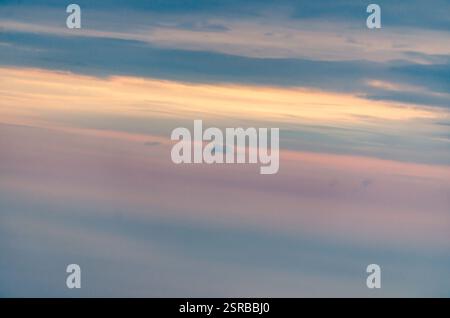 Ampia vista del cielo tranquillo dominato da delicate sfumature pastello durante il tramonto. Le delicate nuvole si allungano, con sottili sfumature di rosa, blu e arancione. Foto Stock