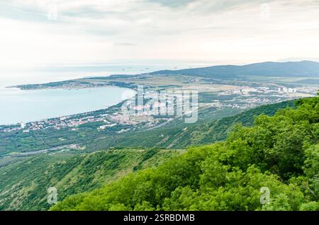 L'ampia vista aerea di Gelendzhik mostra la splendida costa e le lussureggianti colline verdi. L'illuminazione soffusa esalta la vegetazione vibrante e il mare tranquillo. Monte Foto Stock