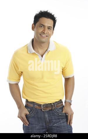 Giovane e sicuro di sé in piedi teneva i pollici nelle tasche dei pantaloni dei jeans indossando una t-shirt gialla MR#703R. Foto Stock