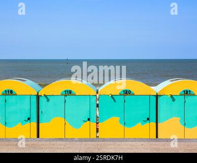 Vivaci capanne da spiaggia gialle e verdi con dettagli dipinti ondulati, adagiate all'orizzonte di un mare calmo. Una vivace e divertente scena costiera ideale per l'estate Foto Stock