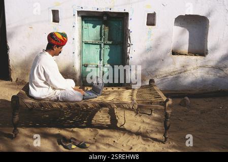 Uomo Rajput che usa un laptop seduto su khat fuori casa, Pushkar, Rajasthan, India, Asia Foto Stock