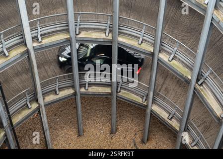 Guardando in basso parte delle rampe circolari di un parcheggio multipiano con un'auto che sale. Febbraio 2025. Foto Stock