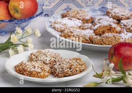 Biscotti d'avena spolverati di zucchero su un piatto circondato da mele e fiori davanti a piastrelle a motivi geometrici Foto Stock