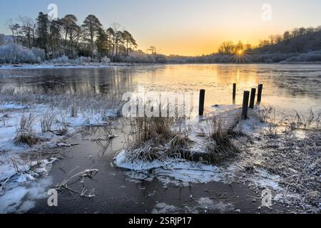 Molo di legno allagato che conduce su un piccolo lago ghiacciato in una fresca mattina invernale. Elterwater, Lake District, Regno Unito. Foto Stock