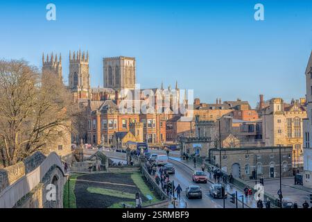 Una vista delle torri di York Minster che si innalzano sopra i tetti della città dalle storiche mura della città. I turisti camminano sul muro, la gente e tra Foto Stock