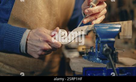 Abile liutaio che realizza un rotolo di violino con precisione e strumenti specializzati in un laboratorio tradizionale, che mostra l'arte della musica fatta a mano Foto Stock