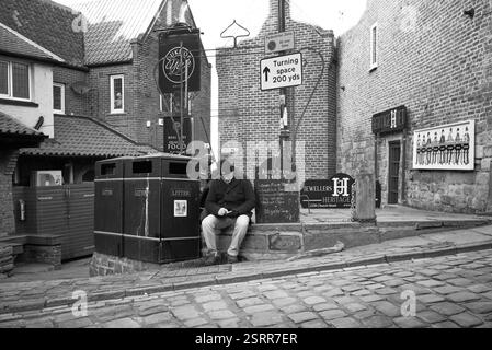 Un uomo anziano seduto a guardare un telefono nella zona di Tate Hill a Whitby Foto Stock