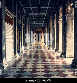 Una galleria storica splendidamente catturata a Venezia, in Italia, caratterizzata da colonne in pietra classiche, intricati dettagli architettonici e un marmo a scacchi Foto Stock