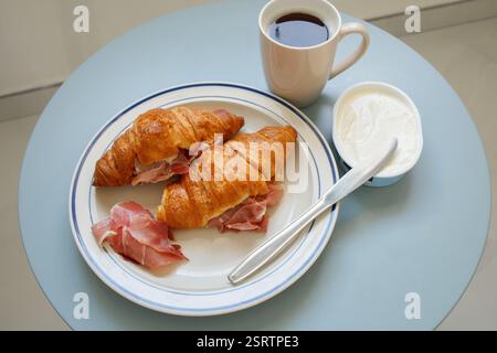 Colazione casalinga: Due croissant con prosciutto, formaggio spalmabile e caffè nero Foto Stock