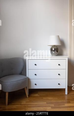 Camera moderna con comò bianco e comoda sedia grigia Foto Stock