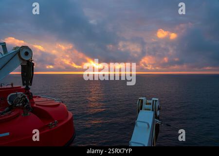 La splendida alba dipinge il cielo con colori vivaci sopra le calme acque dell'oceano. Una scialuppa di salvataggio in primo piano che mette in risalto l'atmosfera marittima Foto Stock