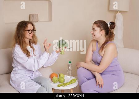 Nutrizionista e giovane donna che discute di mangiare sano, con frutta fresca, broccoli, e un metro a nastro, promuovendo la perdita di peso, la dieta e il benessere i Foto Stock