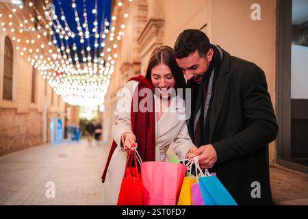 Coppia entusiasta che si diverte a fare shopping insieme mentre aprono colorate borse per lo shopping in una serata gioiosa piena di delizia e attesa mentre esplorano i loro acquisti insieme. Foto di alta qualità Foto Stock
