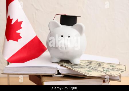 Salvadanaio con soldi e bandiera canadese sui libri vicino al muro luminoso, primo piano. Concetto di prestito per studenti Foto Stock