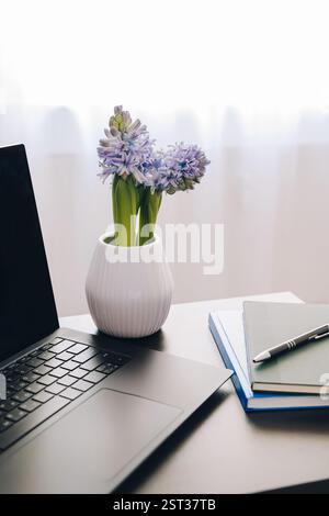 Computer portatile con spazio vuoto per le copie esposto sul tavolo con cancelleria e bouquet di fiori. Sfondo sfocato. Foto Stock