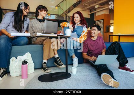 Un gruppo eterogeneo di studenti universitari collabora al lavoro di gruppo in una libreria luminosa, collaborando e condividendo idee utilizzando laptop e. Foto Stock