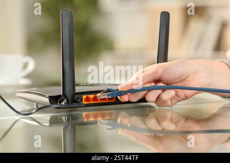 Primo piano di una donna che collega il cavo di rete a un modem sulla scrivania di casa Foto Stock