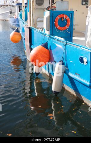 Barca da pesca blu con parafanghi arancioni e salvagente ormeggiato in stile vintage Foto Stock