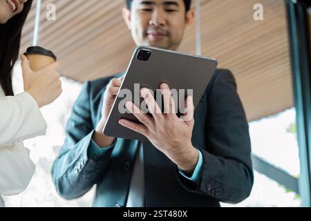 Uomo d'affari che usa un tablet mentre parla con un collega in un ufficio contemporaneo. Foto Stock