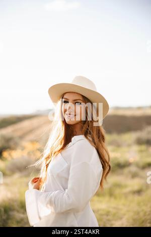 Una giovane donna vibrante con una camicia bianca posa felicemente in un campo erboso Foto Stock