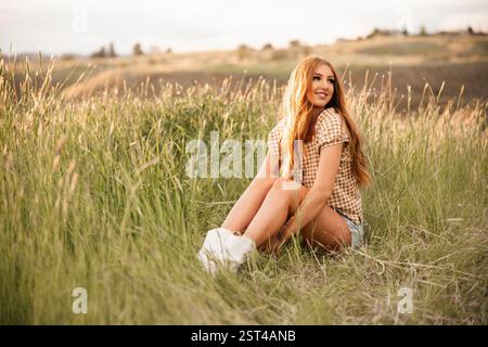 Una giovane donna vibrante siede gioiosamente in un campo erboso. Foto Stock