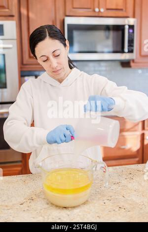 Donna che versa con cura olio d'oliva nella liscivia e nel burro di cacao per ottenere il sapone. Foto Stock