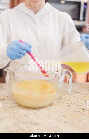 Donna che versa olio d'oliva nel composto di liscivie per il sapone fatto a mano in Stow. Foto Stock