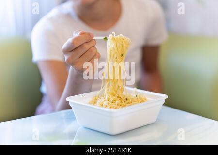 spaghetti istantanei in un contenitore di plastica e una forchetta con una mano rebekah, fast food dannosi Foto Stock