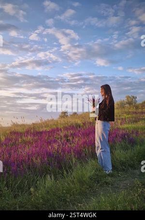 Giovane donna in armonia con la natura che profuma un bouquet di balcanica, fiori di salvia selvatica nel mezzo di un prato viola di Salvia nemorosa. Felice female Foto Stock