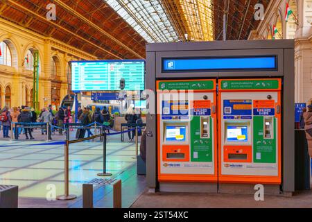 Budapest, Ungheria - 24 novembre 2024: Visualizzazione dei distributori automatici di biglietti, dei viaggiatori impegnati e degli orari dei treni presso la stazione ferroviaria di Buda Foto Stock