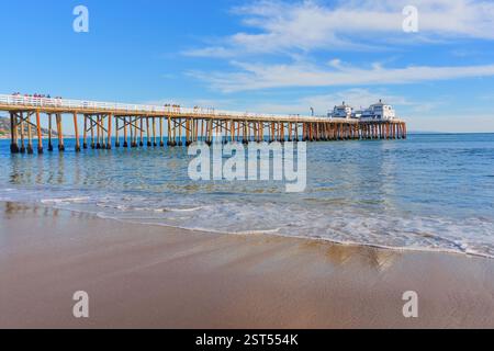 Malibu, California - 29 novembre 2024: Serena vista del Malibu Pier che si estende su acque calme, con dolci onde che lambiscono la spiaggia sabbiosa sotto un riglio Foto Stock