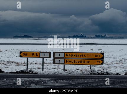 Cartelli stradali direzionali ricoperti di neve con montagne lontane e spettacolari nuvole di tempesta. Foto Stock