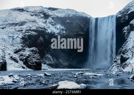 Una foto a lunga esposizione della cascata di Skógafoss in Islanda, dove l'acqua che scorre si trasforma in una cascata di seta sullo sfondo innevato. Foto Stock