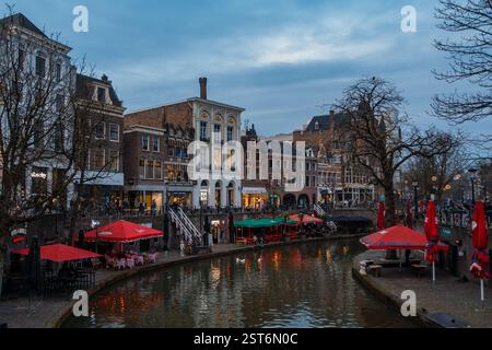 Affascinante scena serale lungo i canali di Utrecht, Paesi Bassi, con architettura storica, accoglienti caffetterie sul lungomare e ombrelloni rossi. Foto Stock