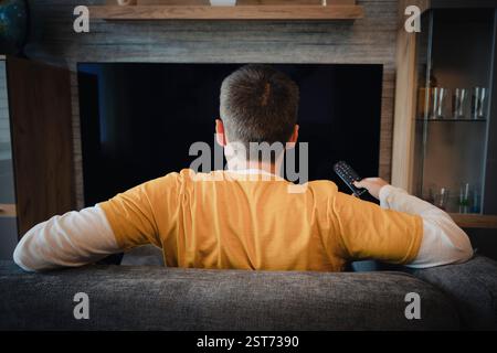 Uomo che guarda la televisione, accende il televisore a schermo piatto al plasma, punta il telecomando verso lo schermo TV vuoto sulla parete bianca. Guy che cambia canale a casa Foto Stock
