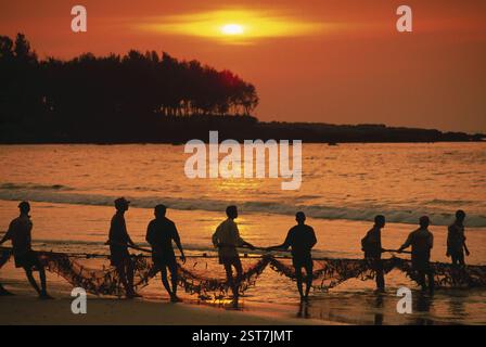 Pescatori che detengono reti al tramonto sulla spiaggia di chiwla, malvan, konkan, maharashtra, india Foto Stock