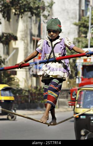 Ragazza asiatica del sud che lavora strada performer equilibrio agire camminando sulla corda con bambù in mano, dopo la performance, i genitori del bambino raccolgono soldi Foto Stock