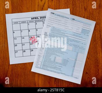 Calendario 2025 aprile giorno fiscale - 15 aprile - in lettere rosse scritte a mano e modulo IRS 1040 seduti su una scrivania di legno Foto Stock