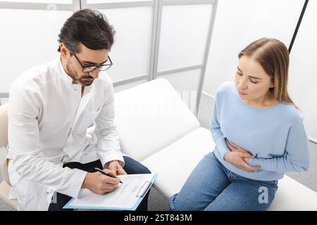 Donna con dolore addominale durante un consulto con gastroenterologa che controlla le condizioni dei suoi organi interni, come stomaco, fegato, gallbladd Foto Stock