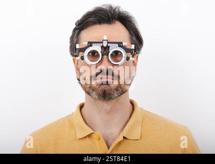 Uomo di mezza età che indossa una montatura di prova optometrista per scegliere gli occhiali per il trattamento della vista, isolata su bianco. Oftalmologia Foto Stock